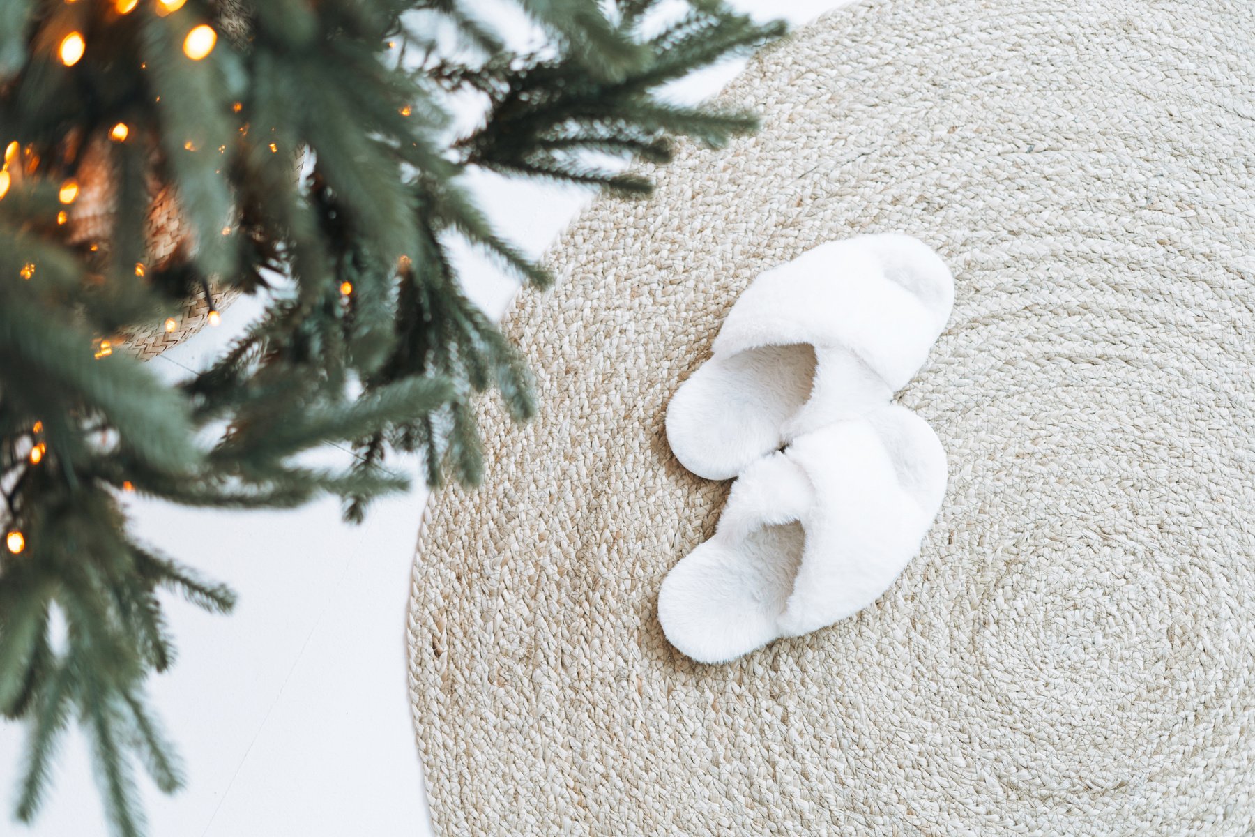 Cozy fluffy slippers on natural rug near Christmas tree, top vie